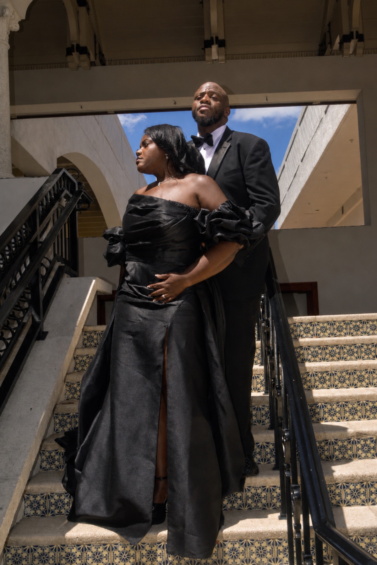 Wilda and Sean standing together on patterned stairs in formal black attire